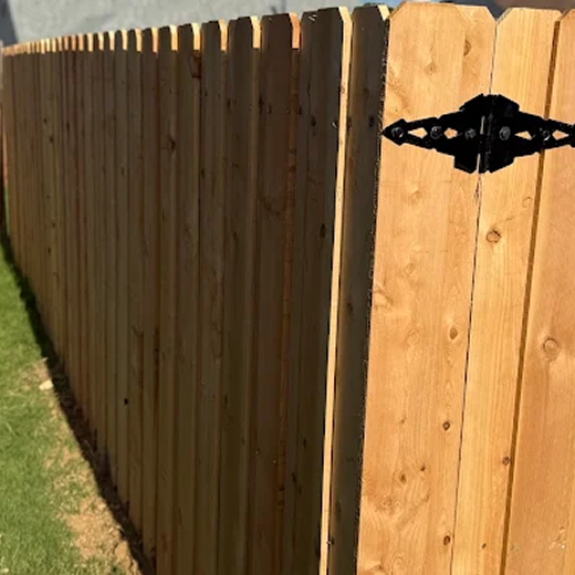 A perspective view of a newly installed cedar privacy fence with dog-ear pickets, featuring a decorative black heavy-duty strap hinge mounted on a gate section, highlighting the clean wood grain and uniform vertical slat alignment along a grassy lawn.