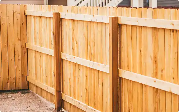 A newly installed wooden privacy fence with vertical planks, showing the posts and horizontal support rails.
