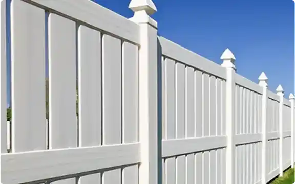 A white vinyl privacy fence with decorative pointed post caps, stretching into the distance against a clear blue sky.